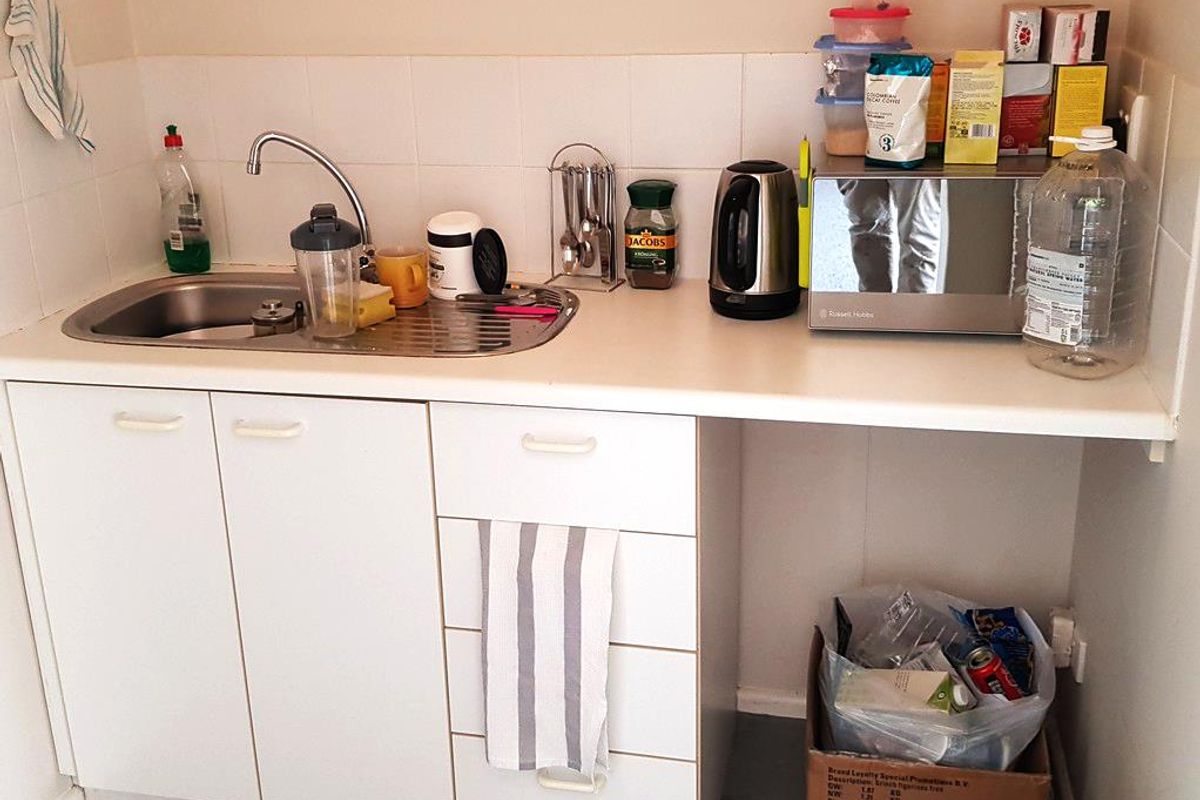 A compact kitchenette area featuring a stainless steel sink, white cabinetry, and tiled splashback, suitable for office tea and coffee preparation.
