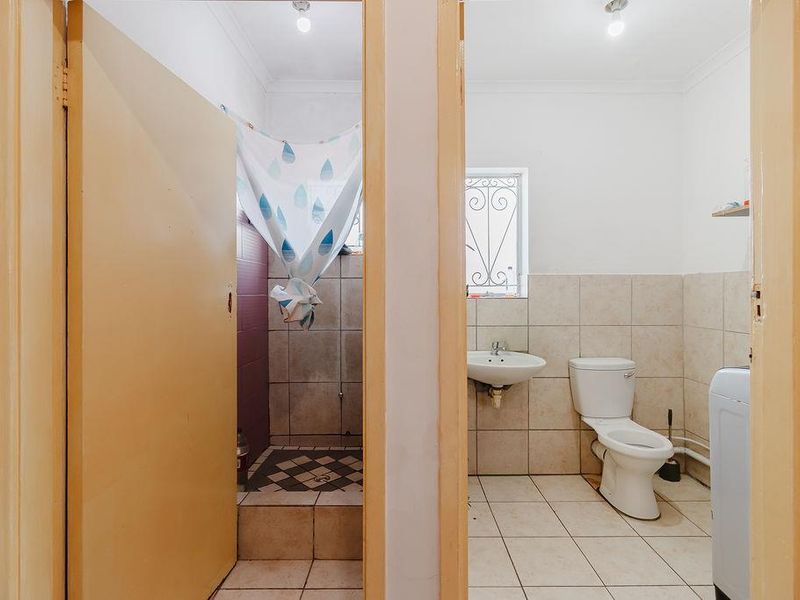 A functional bathroom featuring a toilet, pedestal basin, and a separate shower cubicle with tiled finishes and a security-fitted window.