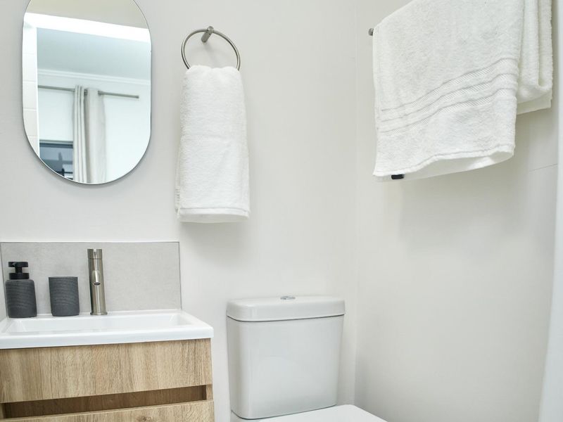 A clean and modern bathroom featuring a wood-finish vanity cabinet, basin, and toilet, complemented by a wall-mounted mirror and towel fixtures.