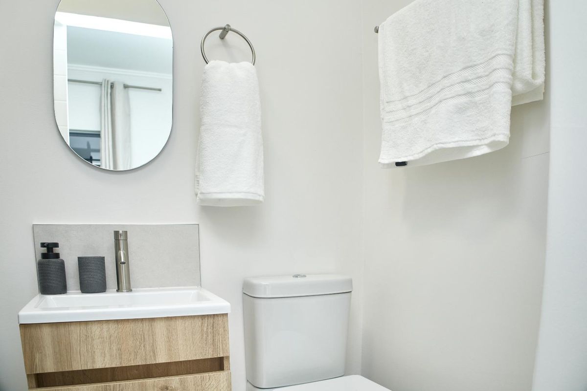 A clean and modern bathroom featuring a wood-finish vanity cabinet, basin, and toilet, complemented by a wall-mounted mirror and towel fixtures.