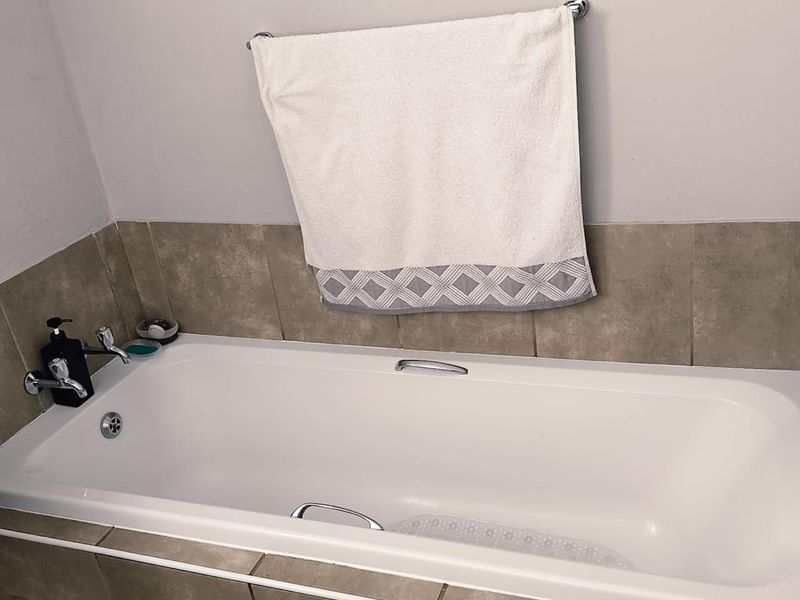 A clean bathroom featuring a built-in bathtub with chrome fixtures and neutral-toned wall tiling.
