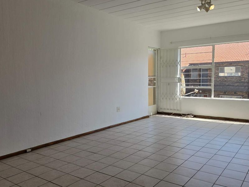 A spacious, empty living area featuring neutral tiled flooring, large windows for natural light, and a security gate leading to an outdoor space.