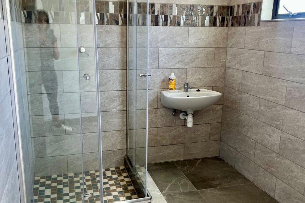 Modern bathroom featuring a glass-enclosed shower, wall-mounted basin, and neutral floor-to-ceiling tiling with a decorative mosaic accent border.