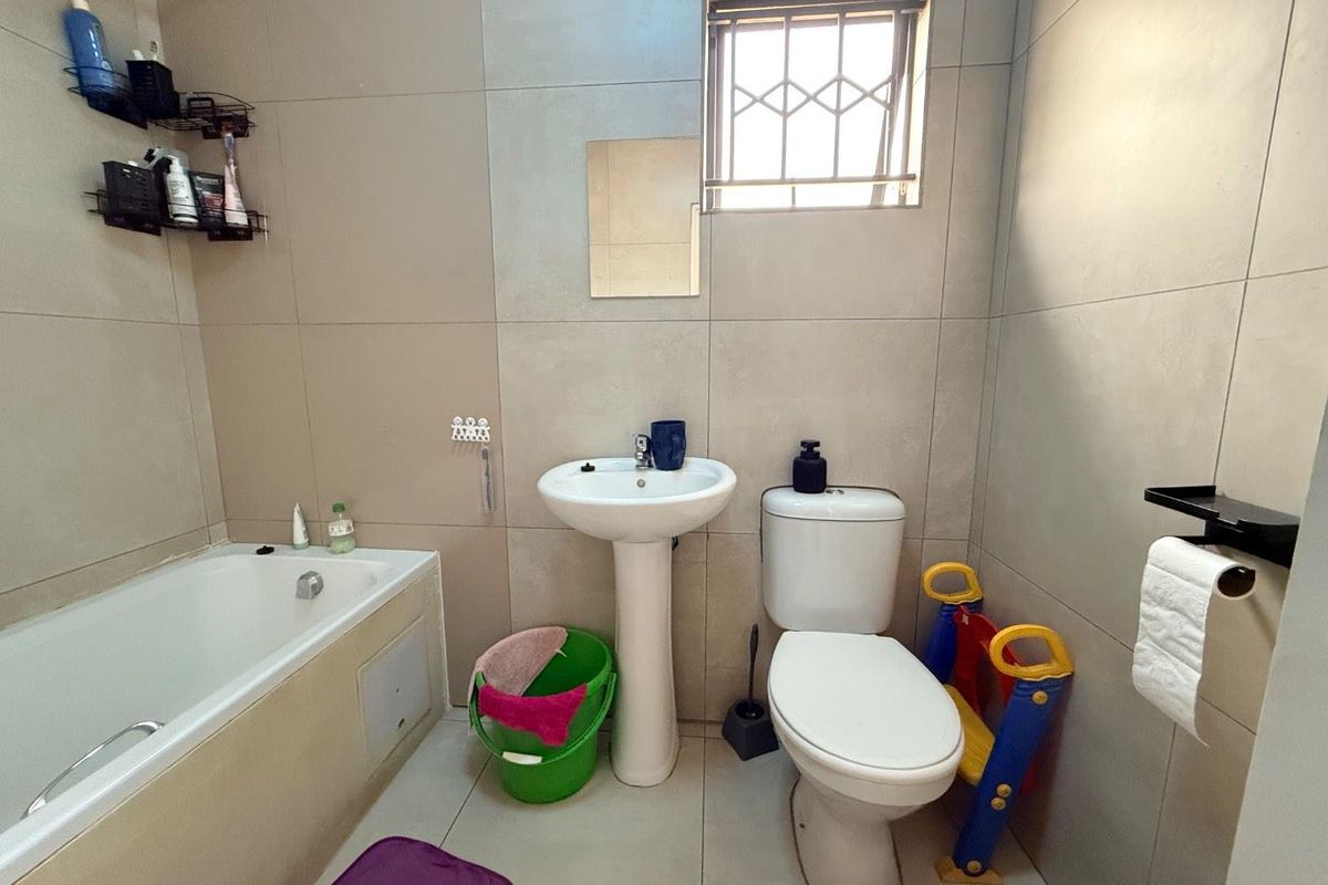 A functional bathroom featuring a bathtub, pedestal basin, and toilet with neutral wall tiling and a small window with security bars.