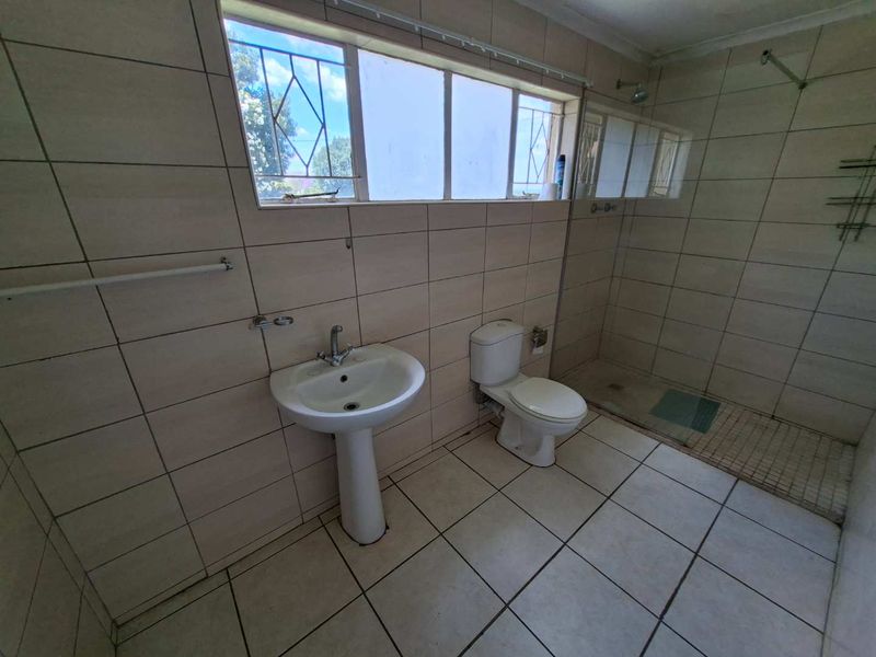 A functional bathroom featuring a pedestal basin, toilet, and walk-in shower with full-height wall tiling and tiled flooring.