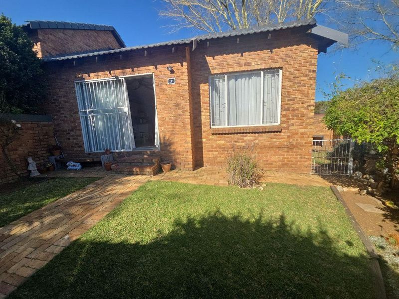 Front view of a face brick townhouse featuring a paved walkway, small garden area, and secure sliding door entrance.