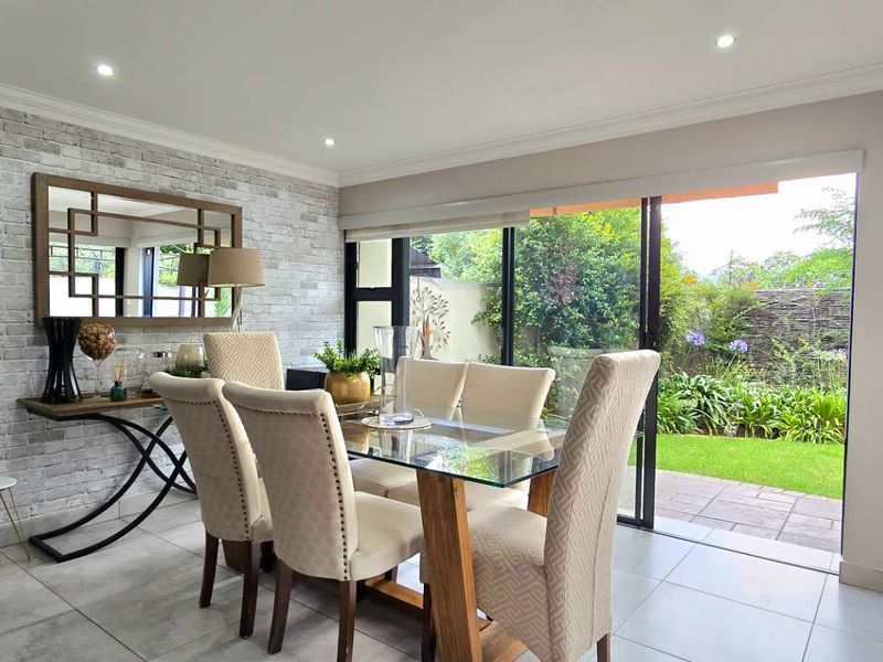 Bright dining room featuring tiled floors, a faux brick accent wall, and large sliding glass doors providing direct access to the garden.