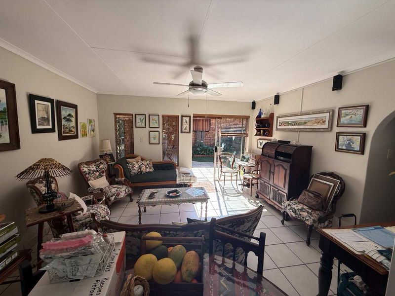 A spacious living room featuring tiled flooring, a ceiling fan, and a sliding glass door providing access to the outdoor patio area.