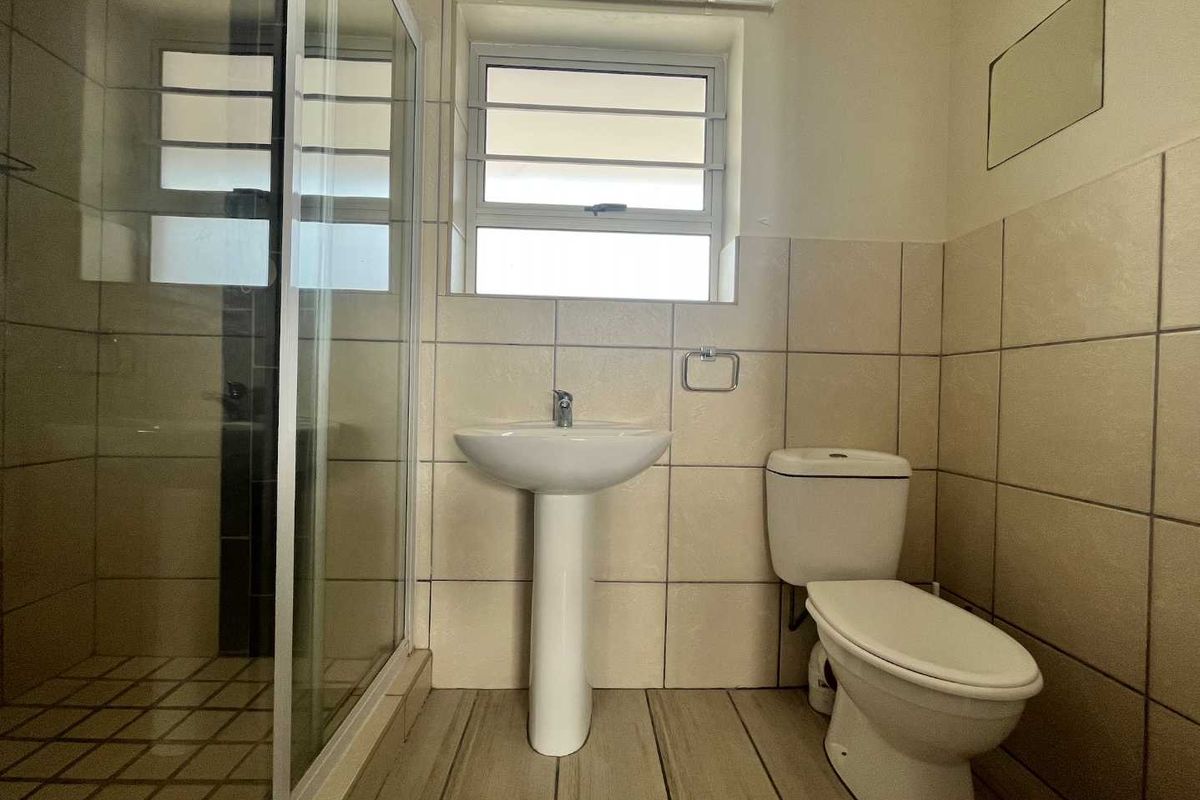A functional bathroom featuring a pedestal basin, toilet, and a glass-enclosed shower with neutral wall and floor tiling.