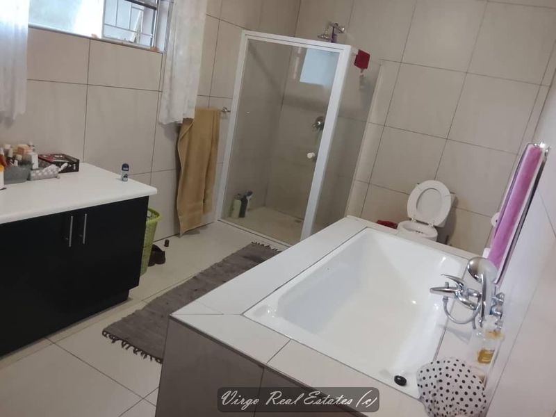 A functional bathroom featuring a built-in bathtub, separate shower enclosure, toilet, and a vanity unit with tiled finishes throughout.