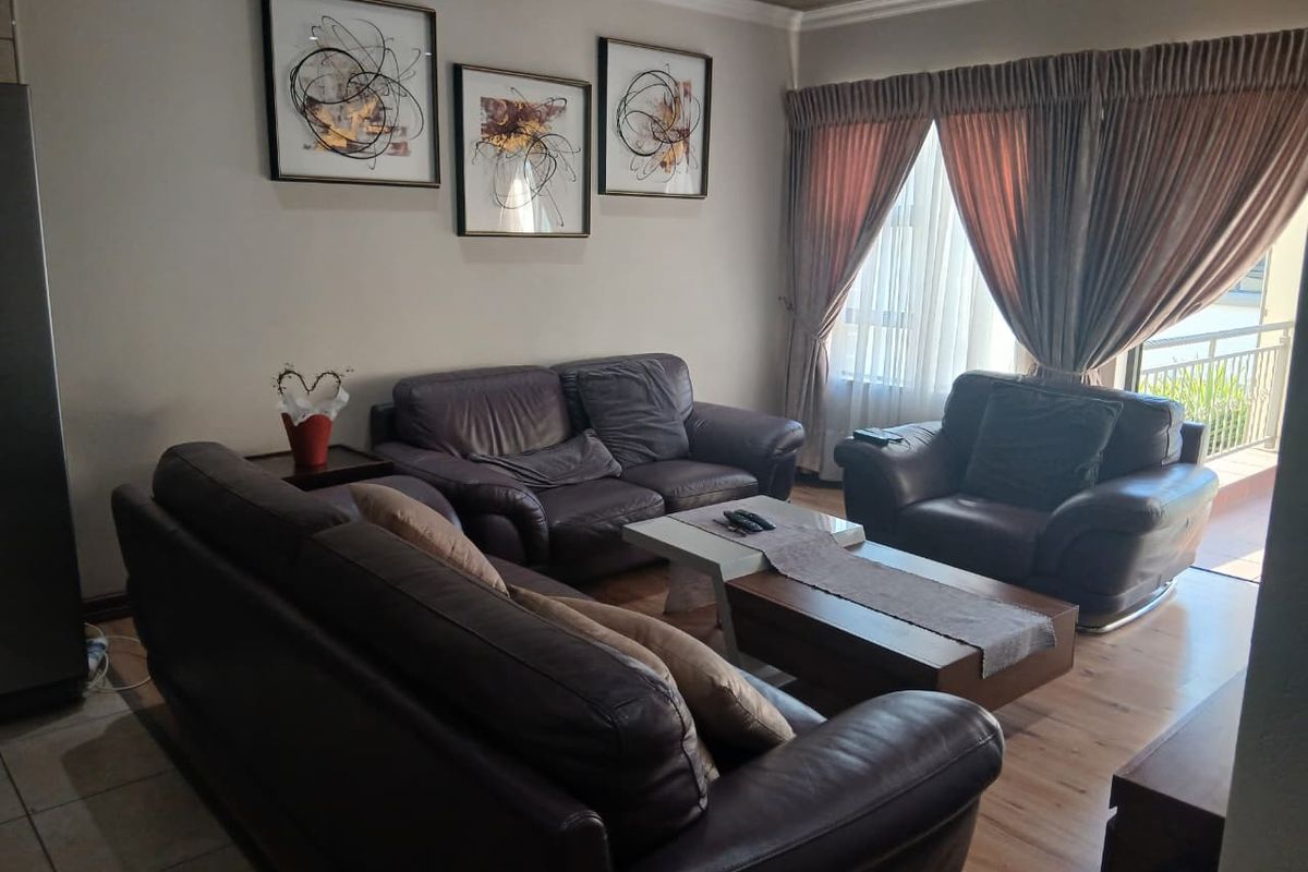 A comfortable living room featuring laminate flooring, recessed ceiling lighting, and a sliding glass door providing access to an outdoor balcony area.
