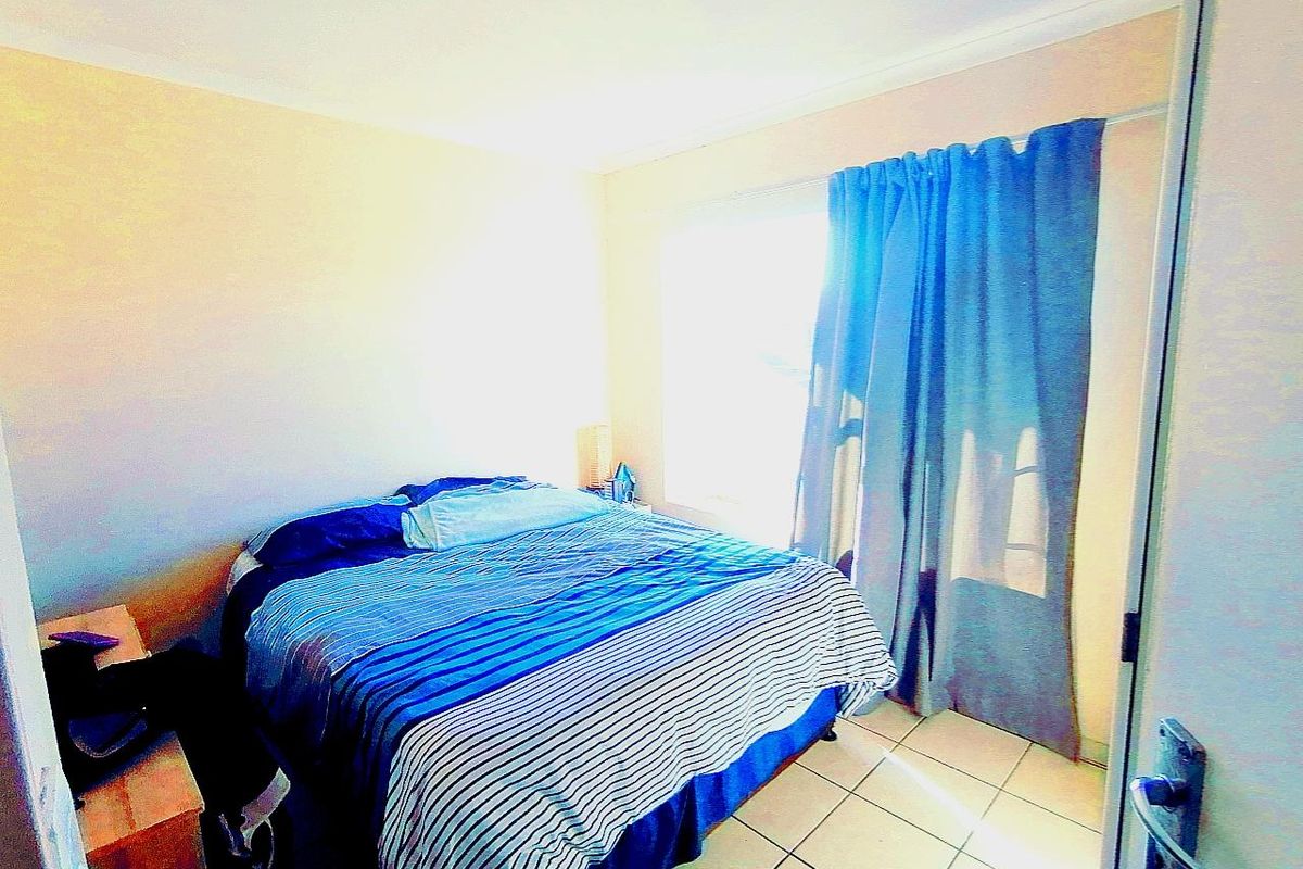 A bedroom featuring tiled flooring and a large window with curtains, providing natural light to the space.