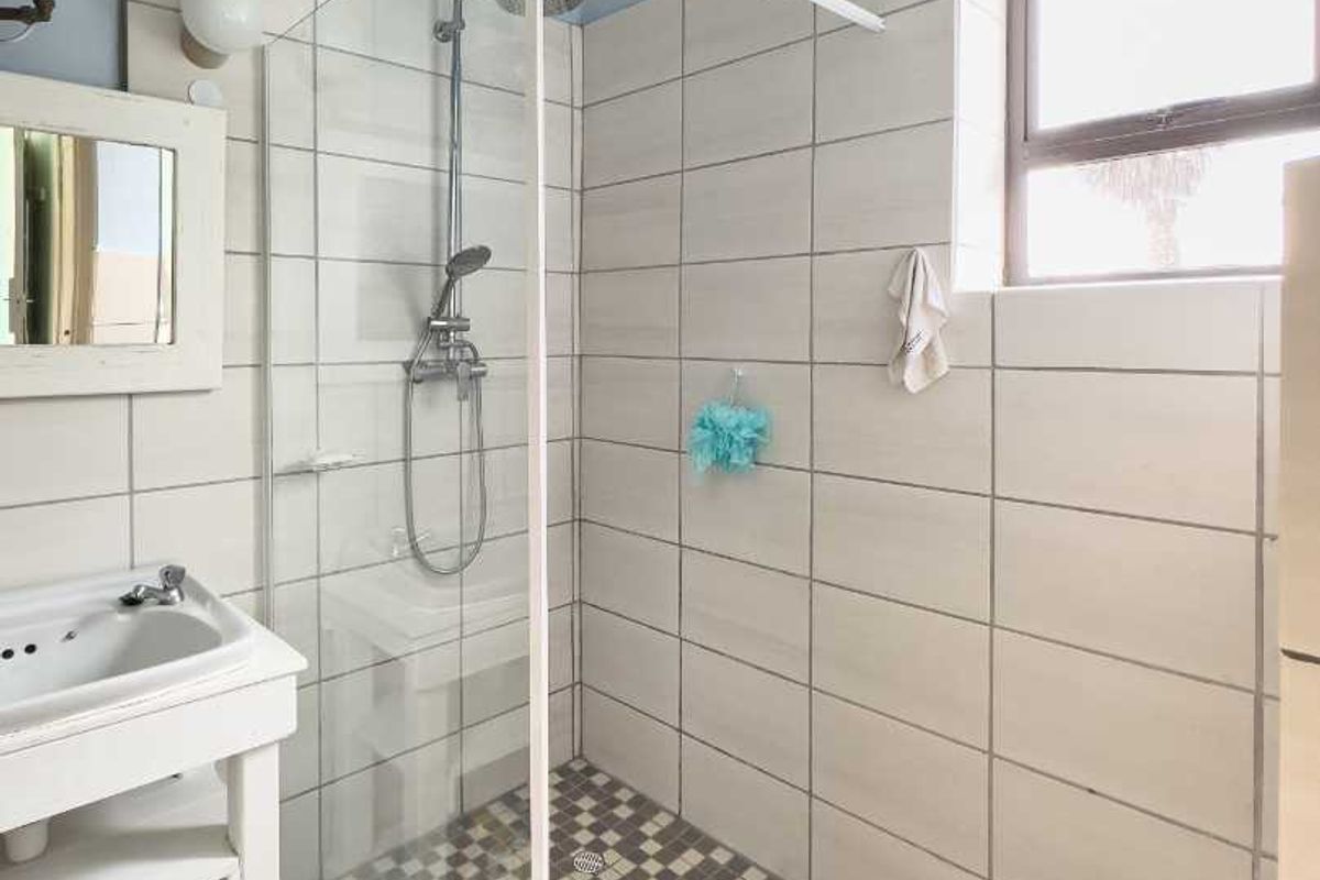 A functional bathroom featuring a walk-in shower with a glass screen, wall-mounted shower head, and a pedestal basin.
