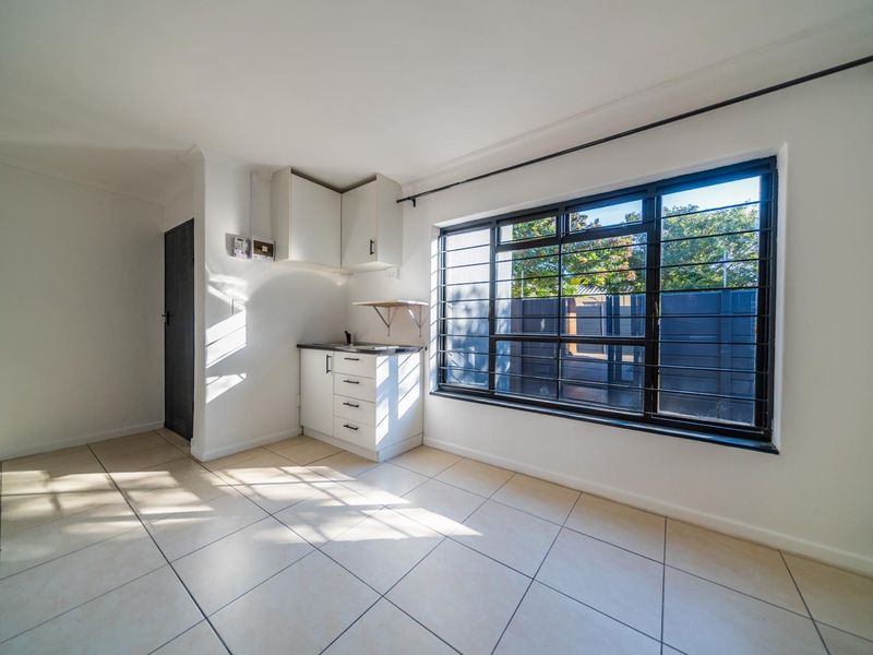 A compact, empty kitchen area featuring tiled flooring, built-in cabinetry, and a large window with security bars.