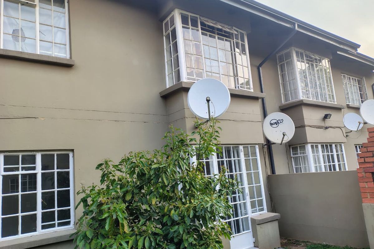 Rear elevation of an apartment building featuring bay windows, security bars, and multiple satellite dishes mounted on the exterior wall.
