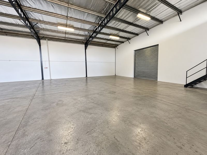 Spacious industrial warehouse unit featuring high ceilings with exposed steel trusses, polished concrete flooring, and a large roller shutter door for easy access.