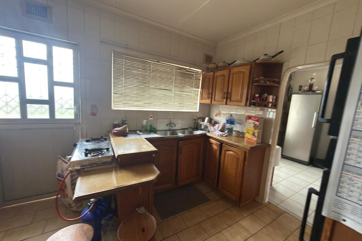 A functional kitchen featuring wooden cabinetry, tiled backsplash, and a double sink, offering potential for modernization and aesthetic updates.