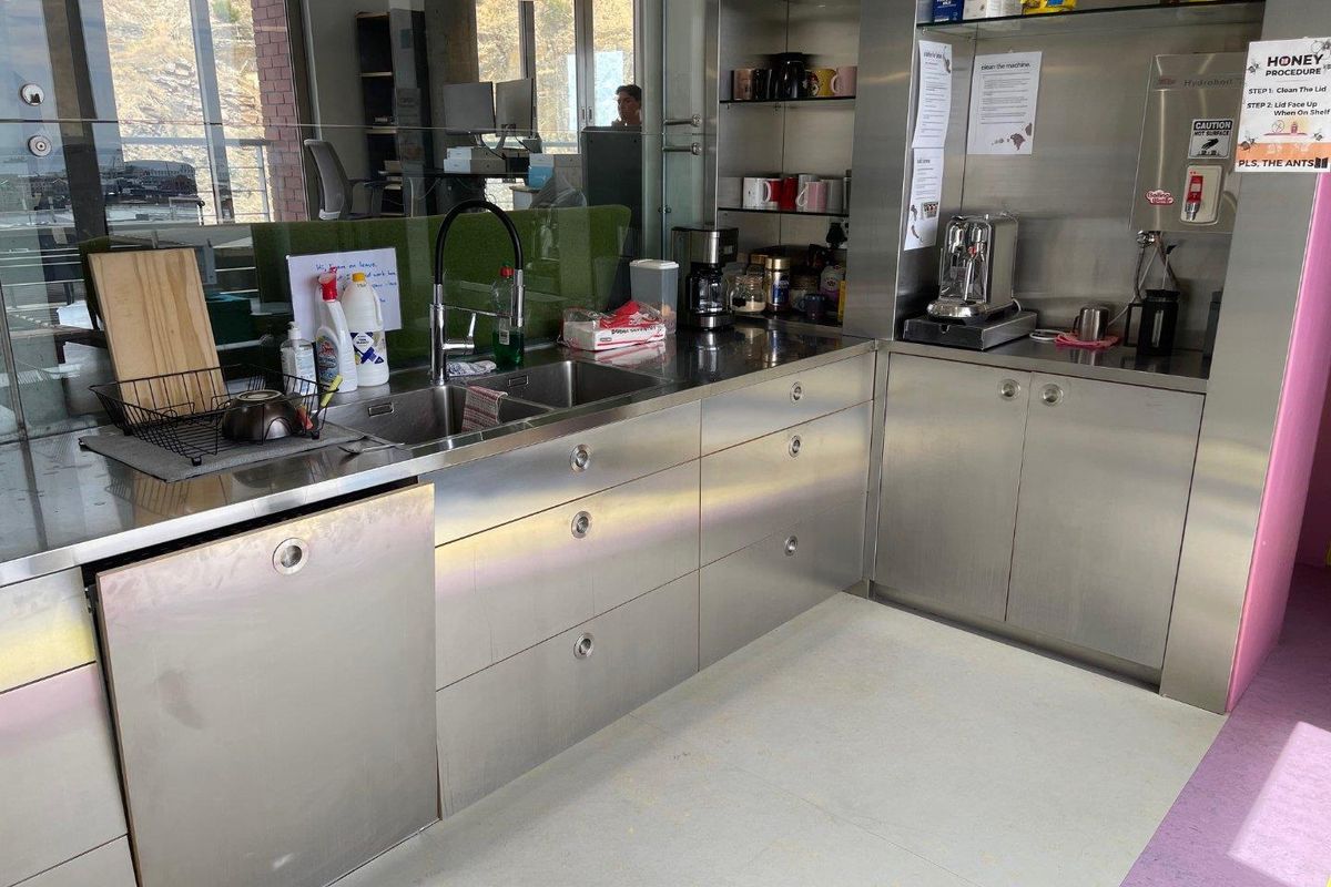 A functional office kitchenette featuring durable stainless steel cabinetry, integrated appliances, and a double bowl sink with a modern mixer tap.