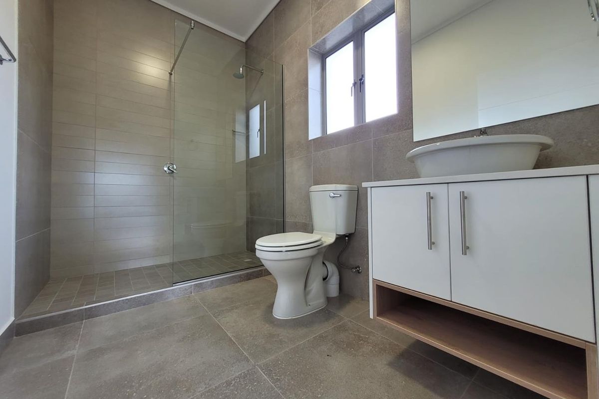 Modern bathroom featuring a glass-enclosed walk-in shower, a contemporary vanity with a vessel sink, and neutral floor-to-ceiling tiling.