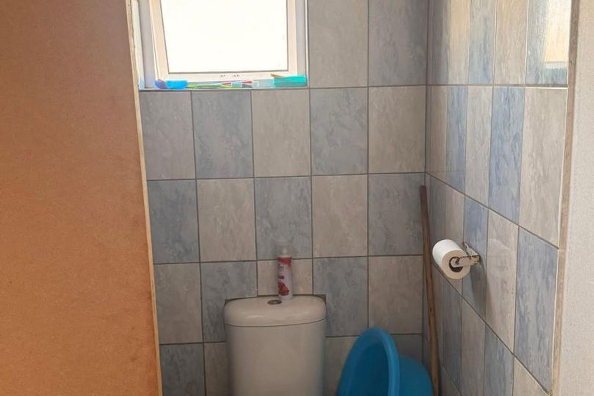 A compact bathroom featuring a standard toilet, tiled walls, and a small window, currently requiring cosmetic updates and finishing touches.