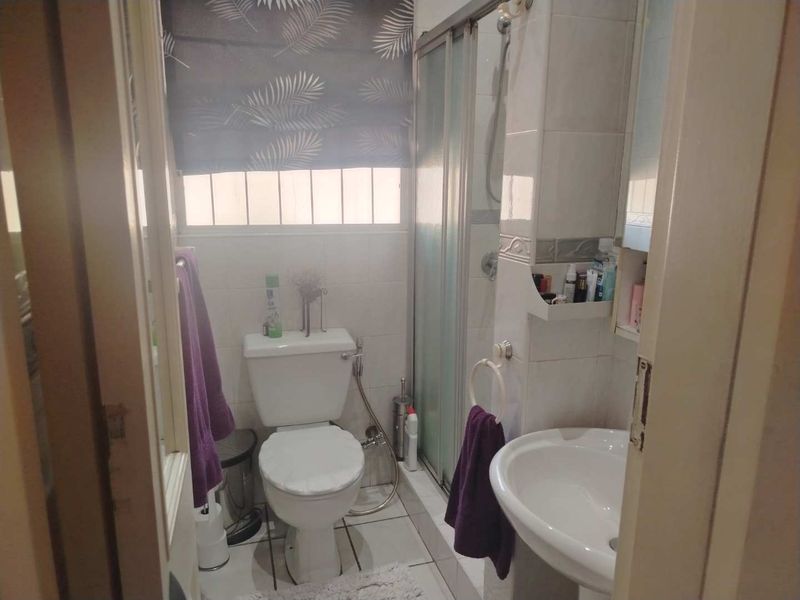 A compact bathroom featuring a shower enclosure, pedestal basin, and toilet with neutral wall and floor tiling.