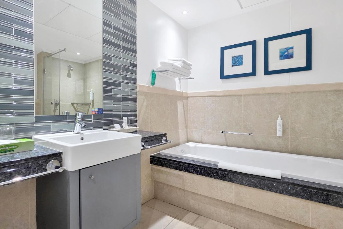 Modern bathroom featuring a vanity with granite countertop, built-in bathtub, and a separate glass-enclosed shower with contemporary tiled accents.
