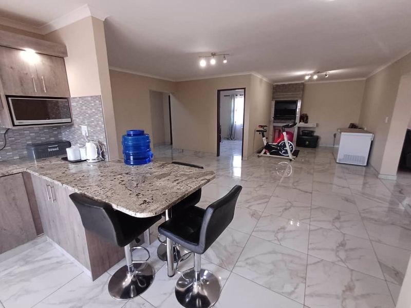 Open-plan living area featuring a modern kitchen with granite countertops, breakfast bar, and tiled flooring throughout, leading to a spacious lounge area.