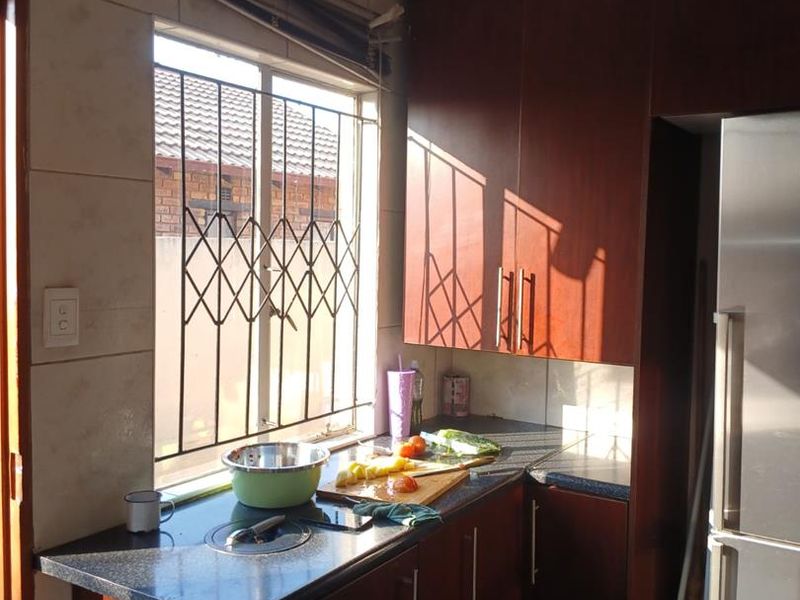 A functional kitchen featuring dark wood cabinetry, laminate countertops, and a window with security bars, providing a practical workspace with natural light.