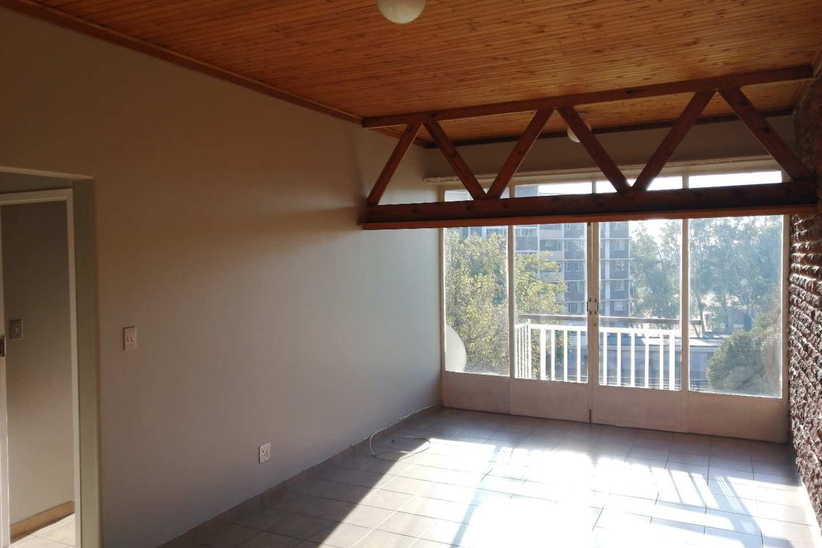 An empty living room featuring a timber ceiling, exposed wooden truss, tiled floors, and an exposed brick wall with access to a balcony.