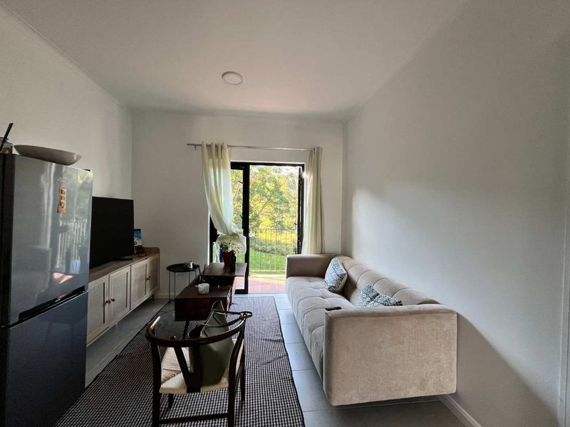 A bright living room featuring tiled flooring and a sliding glass door that opens to an outdoor balcony area.