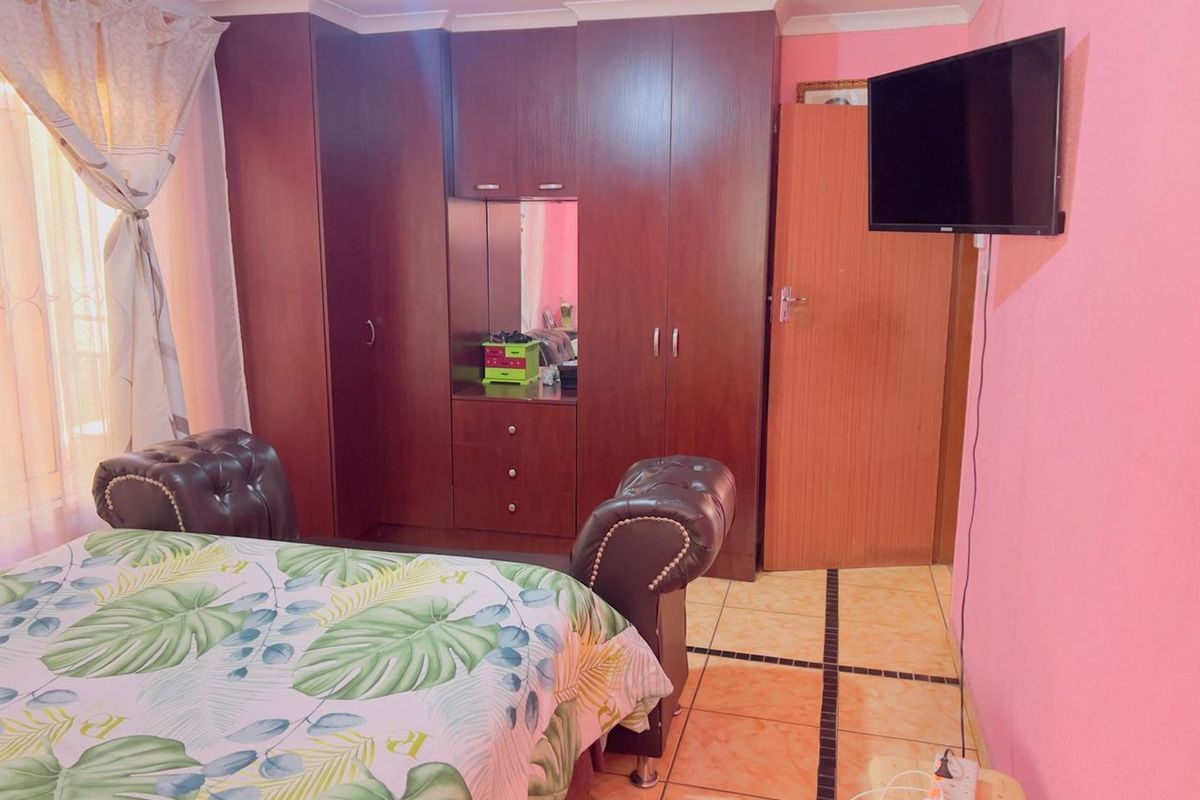 A bedroom featuring built-in wooden cupboards with a central vanity mirror and tiled flooring.
