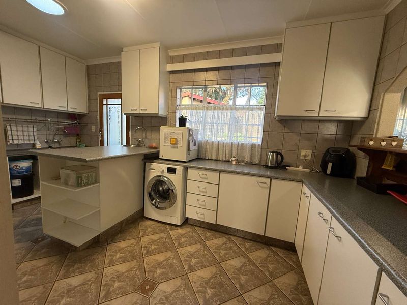 A functional kitchen featuring tiled flooring, ample built-in cabinetry, laminate countertops, and integrated laundry plumbing, offering a practical layout for daily use.
