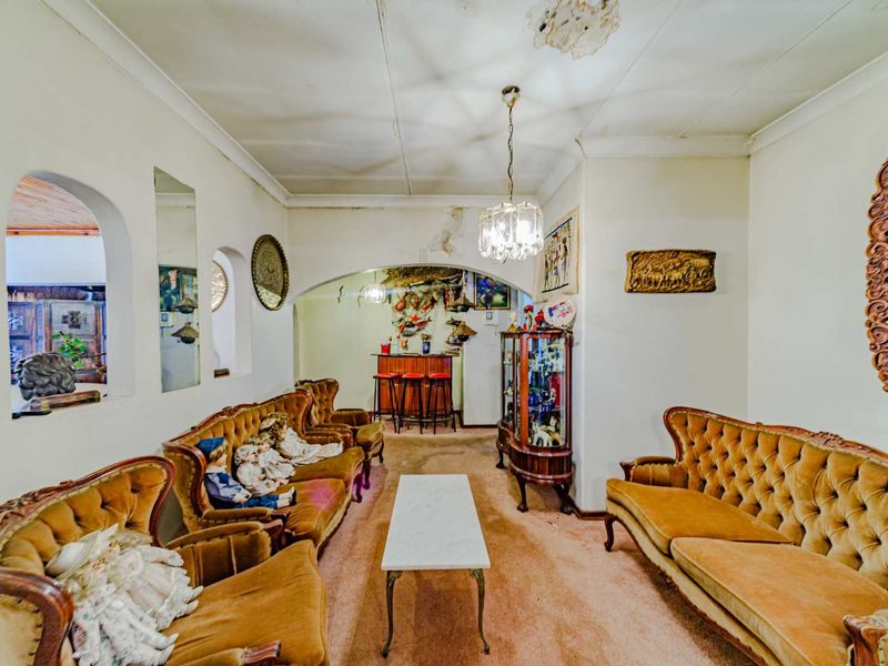 A living room featuring an arched entryway, a built-in bar area, and classic architectural details, currently showing signs of ceiling damage and dated finishes.