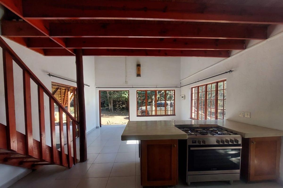 Spacious open-plan living and kitchen area featuring exposed timber beams, a wooden staircase, tiled floors, and a functional kitchen with a concrete countertop.