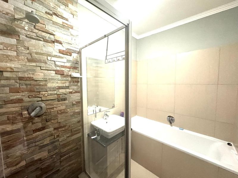 Modern bathroom featuring a stone-clad shower wall, glass enclosure, built-in bathtub, and a vanity basin with storage cabinet.
