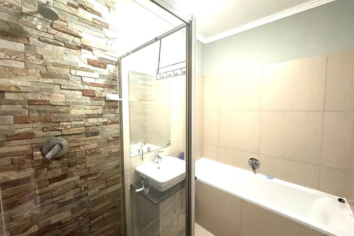 Modern bathroom featuring a stone-clad shower wall, glass enclosure, built-in bathtub, and a vanity basin with storage cabinet.