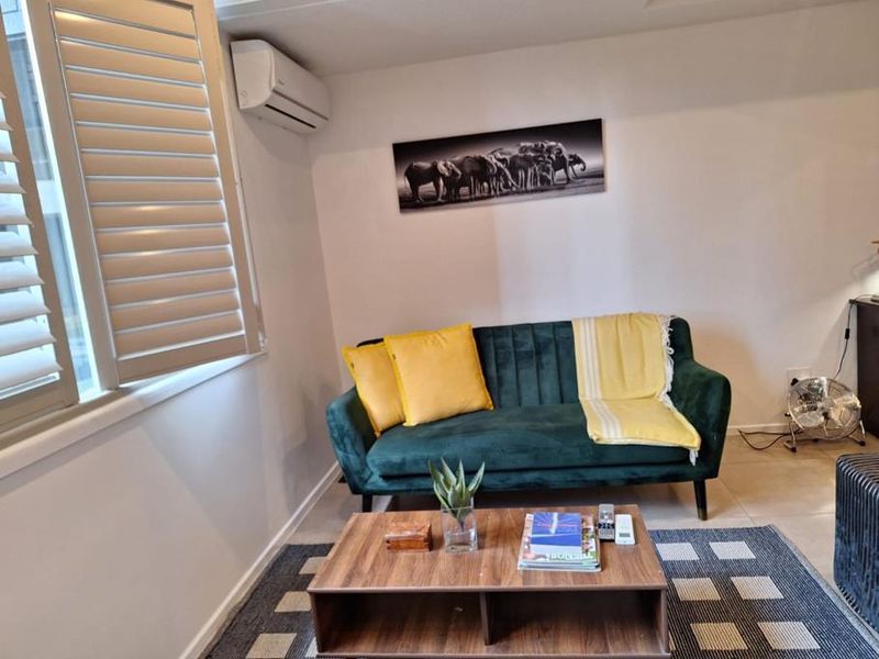A comfortable living room featuring tiled flooring, plantation shutters for light control, and a wall-mounted split-system air conditioning unit.