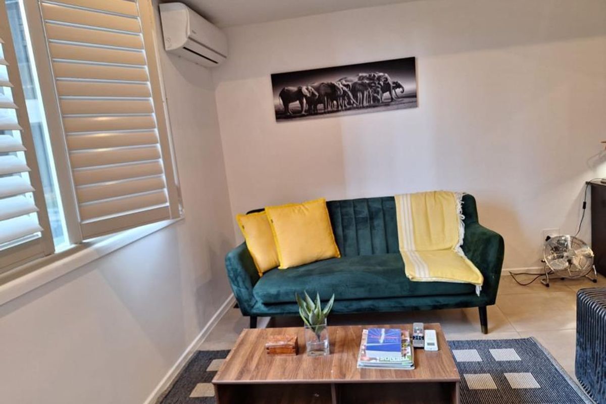 A comfortable living room featuring tiled flooring, plantation shutters for light control, and a wall-mounted split-system air conditioning unit.