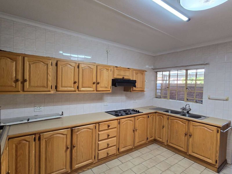 A functional kitchen featuring traditional wooden cabinetry, laminate countertops, a built-in gas hob, and a double stainless steel sink with tiled splashbacks.