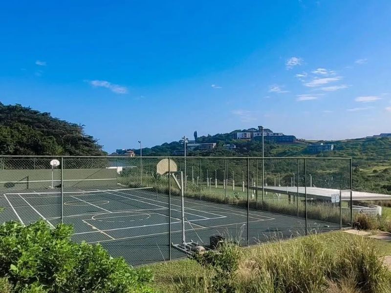 A well-maintained outdoor sports facility featuring a fenced tennis court with integrated basketball hoops and floodlight infrastructure.