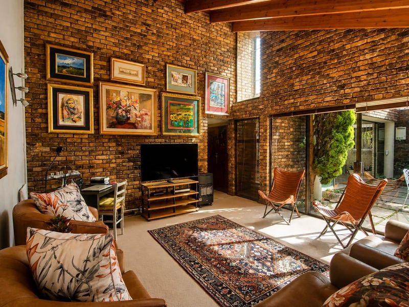 Spacious living room featuring exposed brick walls, high timber-beamed ceilings, and large sliding glass doors that provide seamless access to the outdoor patio area.