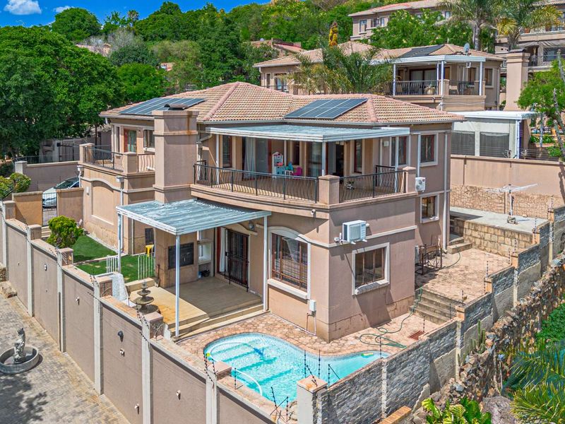 Aerial view of a multi-level residential property featuring a swimming pool, patio, balcony, solar panels, and secure perimeter walling.