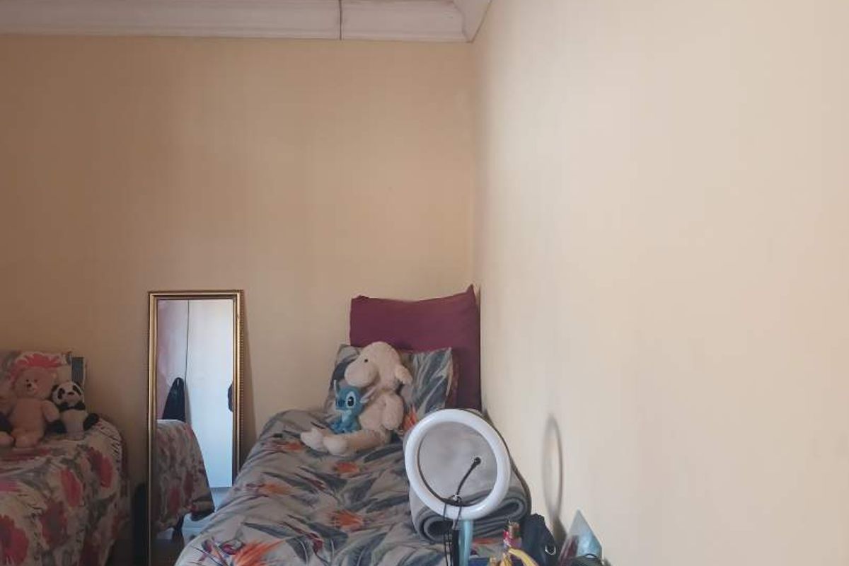 A bedroom featuring plain walls and a visible ceiling crack in the corner, indicating potential maintenance requirements.
