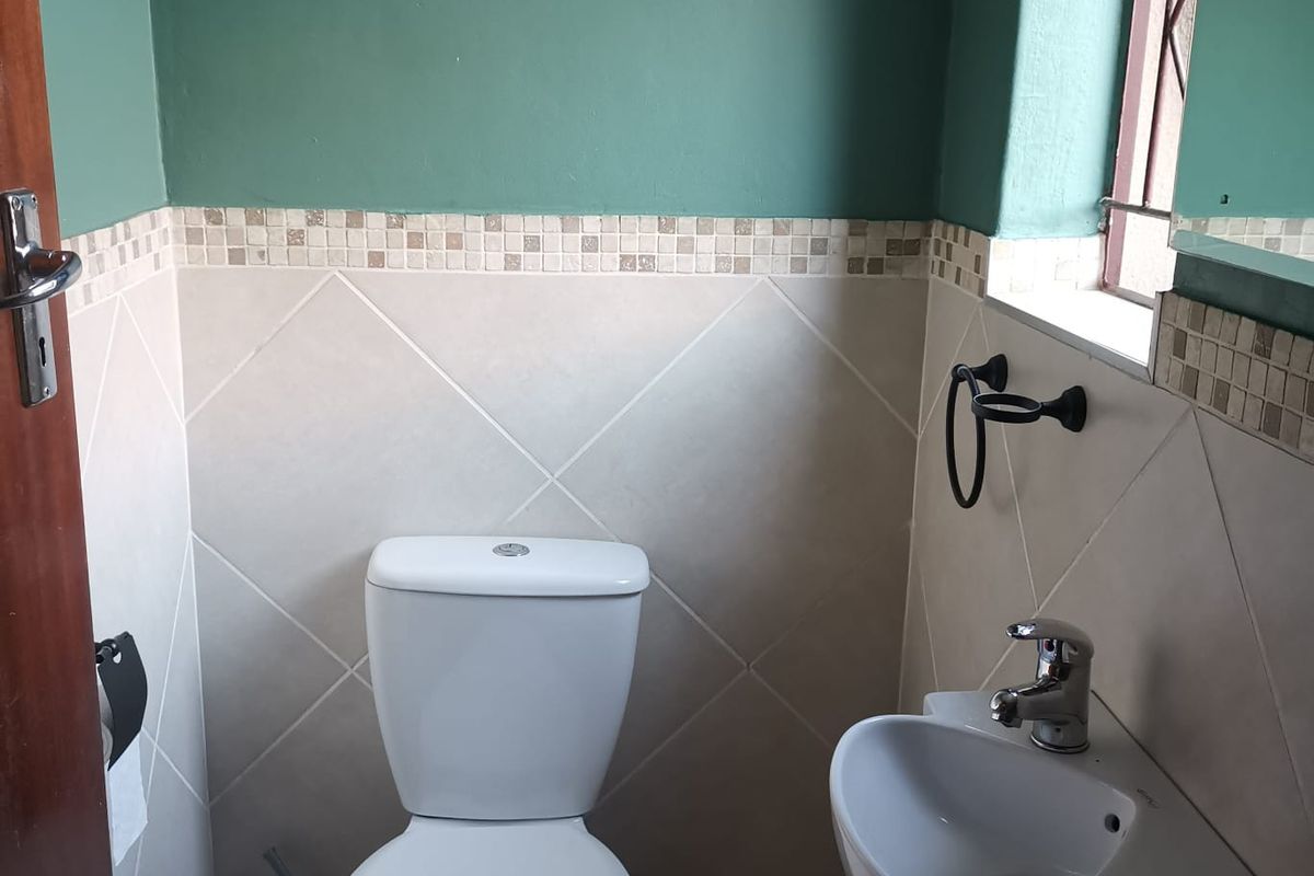 A compact guest bathroom featuring a white toilet, wall-mounted basin with mixer tap, and neutral wall tiling with a decorative mosaic border.