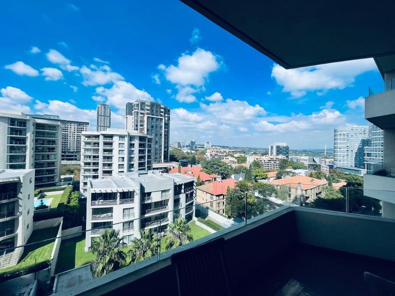 A modern apartment balcony featuring a sleek glass balustrade and offering expansive elevated views of the surrounding urban landscape.