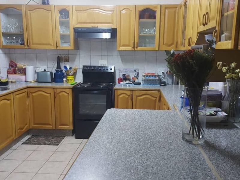 A functional kitchen featuring wooden cabinetry, granite-look laminate countertops, a tiled backsplash, and a freestanding stove with an extractor fan.