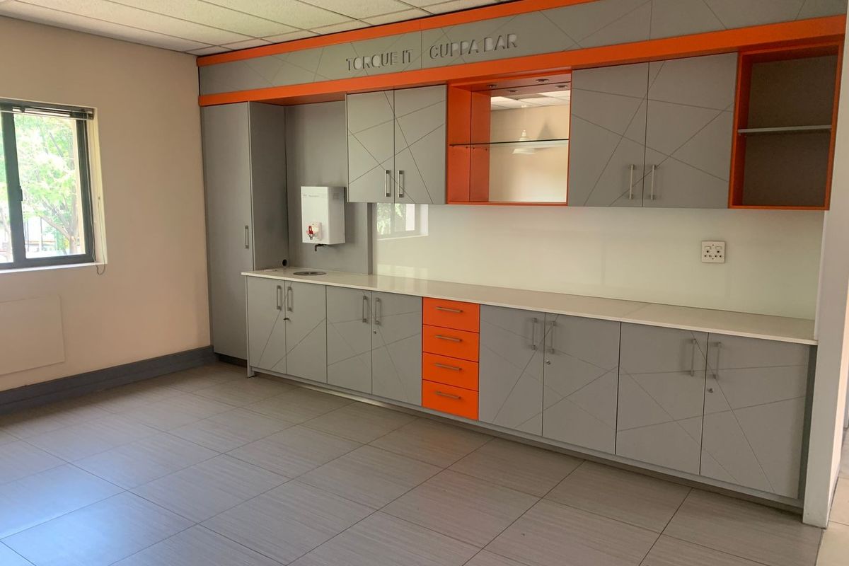 A modern office kitchenette featuring custom grey and orange cabinetry, integrated shelving, a built-in water dispenser, and tiled flooring.