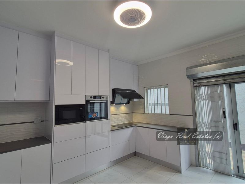 Modern kitchen featuring high-gloss white cabinetry, integrated appliances, sleek tiled flooring, and direct access to an outdoor area through a secure sliding door.