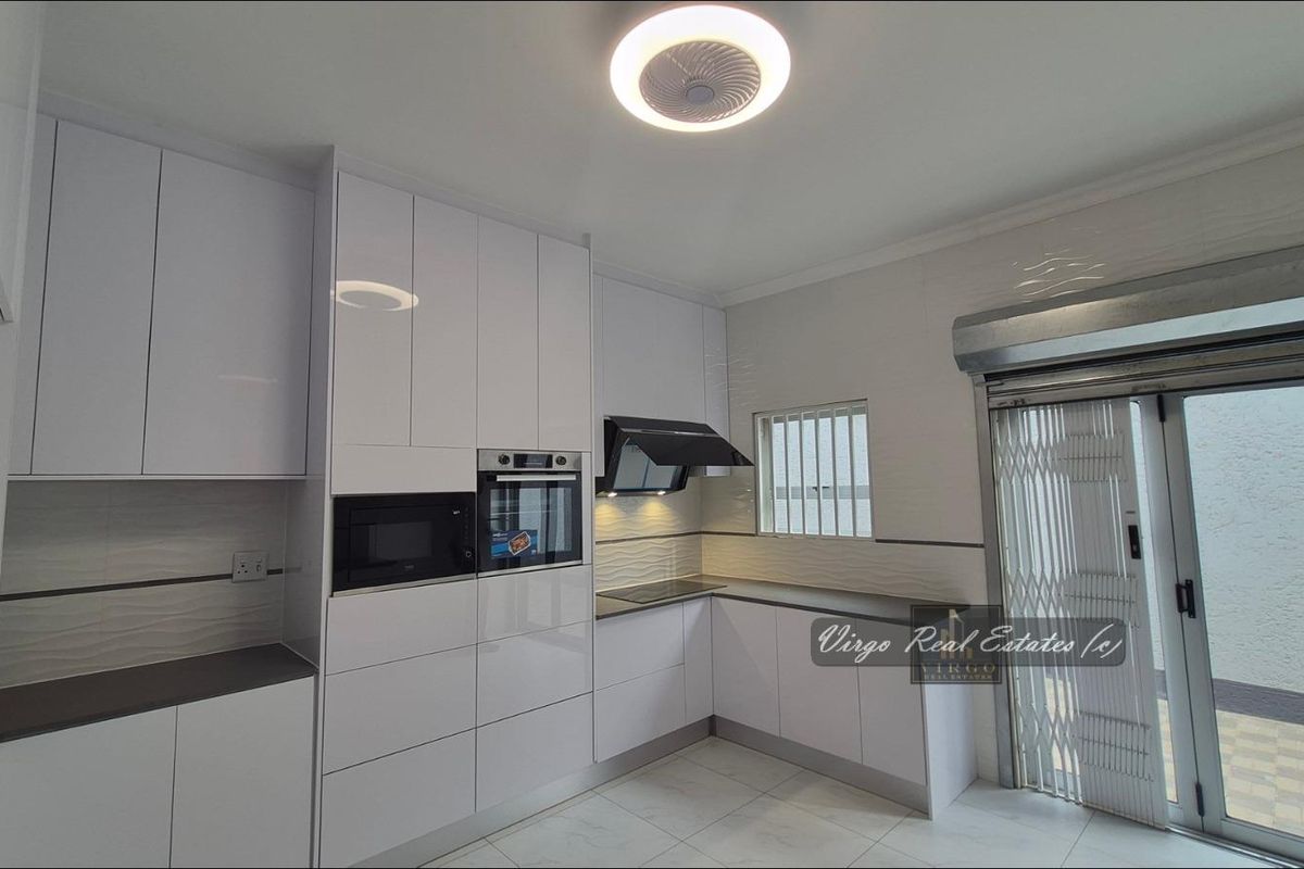 Modern kitchen featuring high-gloss white cabinetry, integrated appliances, sleek tiled flooring, and direct access to an outdoor area through a secure sliding door.