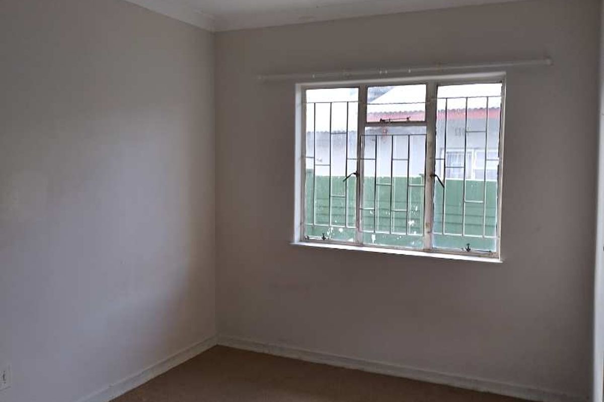 An empty bedroom featuring neutral walls, carpet flooring, and a window fitted with security bars.